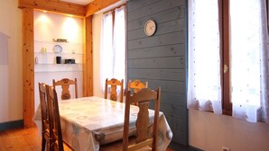 Ein Esszimmer mit Holztisch und Stühlen, einer Wanduhr und einem Fenster mit Vorhängen.