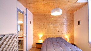 Ein Schlafzimmer mit Holzboden, einer Bett mit grauer Bettdecke, Nachttischlampen und einer Holzzieldecke.