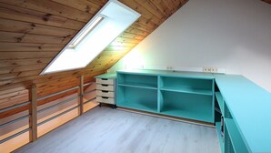 Ein Zimmer mit schräg verlegter Decke, einem Oberlicht, einem türkisblauen Schreibtisch und einer weißen Wand.