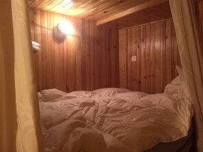 Ein Zimmer mit Holzwandverkleidung, einem Bett, einer Wandleuchte und einer Steckdose.