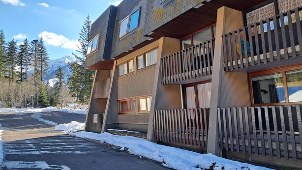 Um edifício com vários andares, varandas, área de estacionamento e neve no chão.