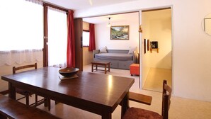 Uma área de refeições com uma mesa de madeira, cadeiras e uma tigela. Há um sofá e um quadro ao fundo.