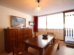 A dining area with a wooden table, chairs, a bench, a television on a stand, a painting on the wall, and a window with curtains. - F2 at the slopes with balcony and parking - 6 people (Mont-Dore)
