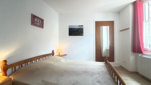 A bedroom with a bed, a nightstand, a lamp, a mirror, a door, and a window with curtains. - F2 with WIFI downtown near spa (Mont-Dore)