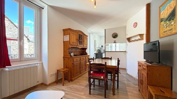 A cozy kitchen with wooden cabinets, a dining table, and a TV. - F2 with WIFI downtown near spa (Mont-Dore)