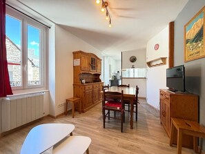 A cozy kitchen with wooden cabinets, a dining table, and a TV. - F2 with WIFI downtown near spa (Mont-Dore)
