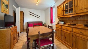 A room with a wooden dining table, a television, a bed with red pillows, and wooden cabinets. - F2 with WIFI downtown near spa (Mont-Dore)