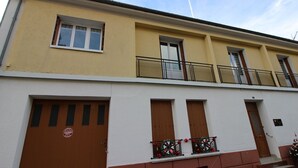 Een gebouw met twee verdiepingen, een gele gevel, een wit gedeelte beneden en een balkon met metalen hekwerk.