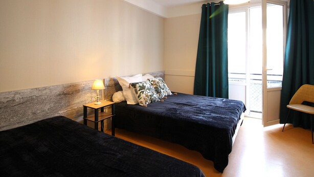 Een hotelkamer met twee bedden, een tafeltje met een lamp, een stoel en uitzicht naar buiten door een raam met gordijnen.