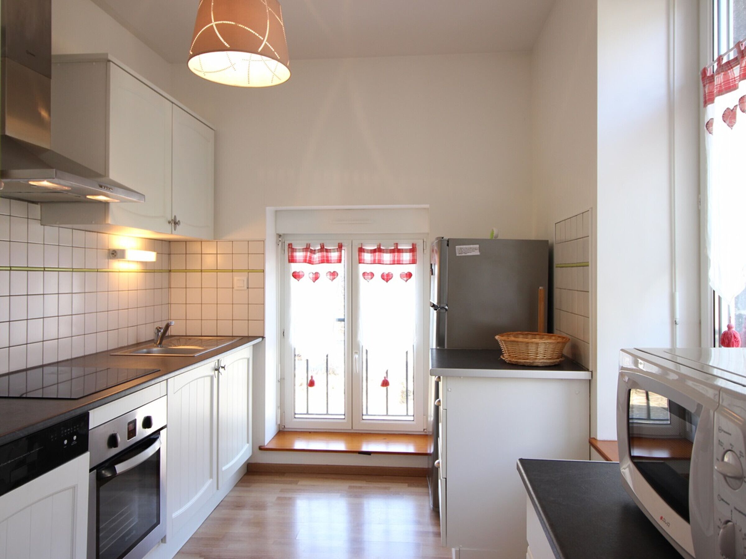Una cocina compacta con armarios blancos, horno empotrado, refrigerador y microondas.