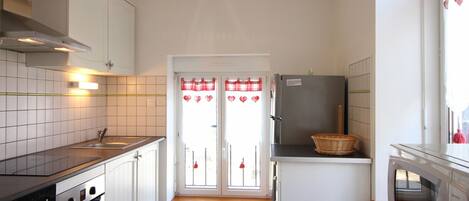 Una cocina compacta con armarios blancos, horno empotrado, refrigerador y microondas.