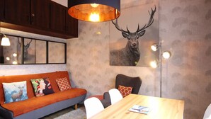 Uma sala de estar moderna com uma mesa de jantar de madeira, um sofá com almofadas estampadas e uma grande obra de arte de um veado na parede.