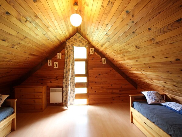 A cozy attic bedroom with wooden walls, a sloped ceiling, and a skylight. There are two beds with pillows and a small dresser.