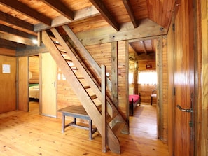 A wooden cabin interior with a wooden staircase, a bed, and a chair.