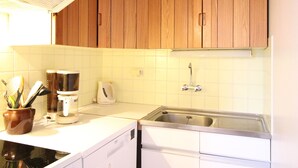A kitchen with wooden cabinets, a white countertop, a coffee maker, a kettle, and a stainless steel sink. - Spacious duplex in Mont-Dore with private parking (Mont-Dore)