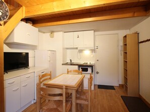 Une cuisine compacte avec des meubles blancs, une table à manger avec des chaises, un four à micro-ondes et un téléviseur posé sur un meuble blanc.