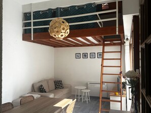 Ein kompakter Wohnraum mit Schlafgalerie, einer Couch, einem Esstisch und einer Leitern.