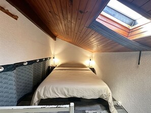 A narrow room with a sloped ceiling, a bed, and two wall-mounted lamps.