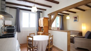 Eine gemütliche Küche mit Holzbalken, einem Esstisch und einer Couch in einem hellen Raum mit großen Fenstern.