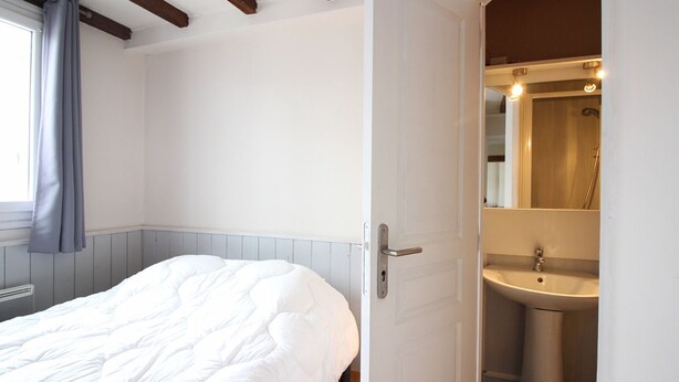 Ein Schlafzimmer mit Bett, ein Badezimmer mit Waschbecken und Spiegel sowie ein Fenster mit Vorhängen.
