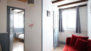 Ein Zimmer mit einem roten Sofa, einer Holzbalkendecke, einem Fenster mit Vorhängen und einer Tür zu einem anderen Raum.