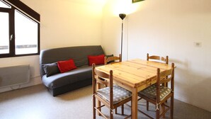 A cozy room with a wooden dining table, four chairs, a grey sofa with red cushions, and a window providing natural light. - Studio at Mont-Dore slopes, 4 pers. (Mont-Dore)