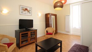 A living room with a television, a cabinet, a wicker chair, a sofa, and a table. - F2 Apartment with terrace and garden, near Mont-Dore center (Mont-Dore)