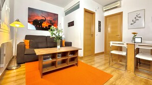 A living room with a sofa, a wooden coffee table, a lamp, and a painting on the wall. - Alaia Gran Via Seasonal Living (Madrid)