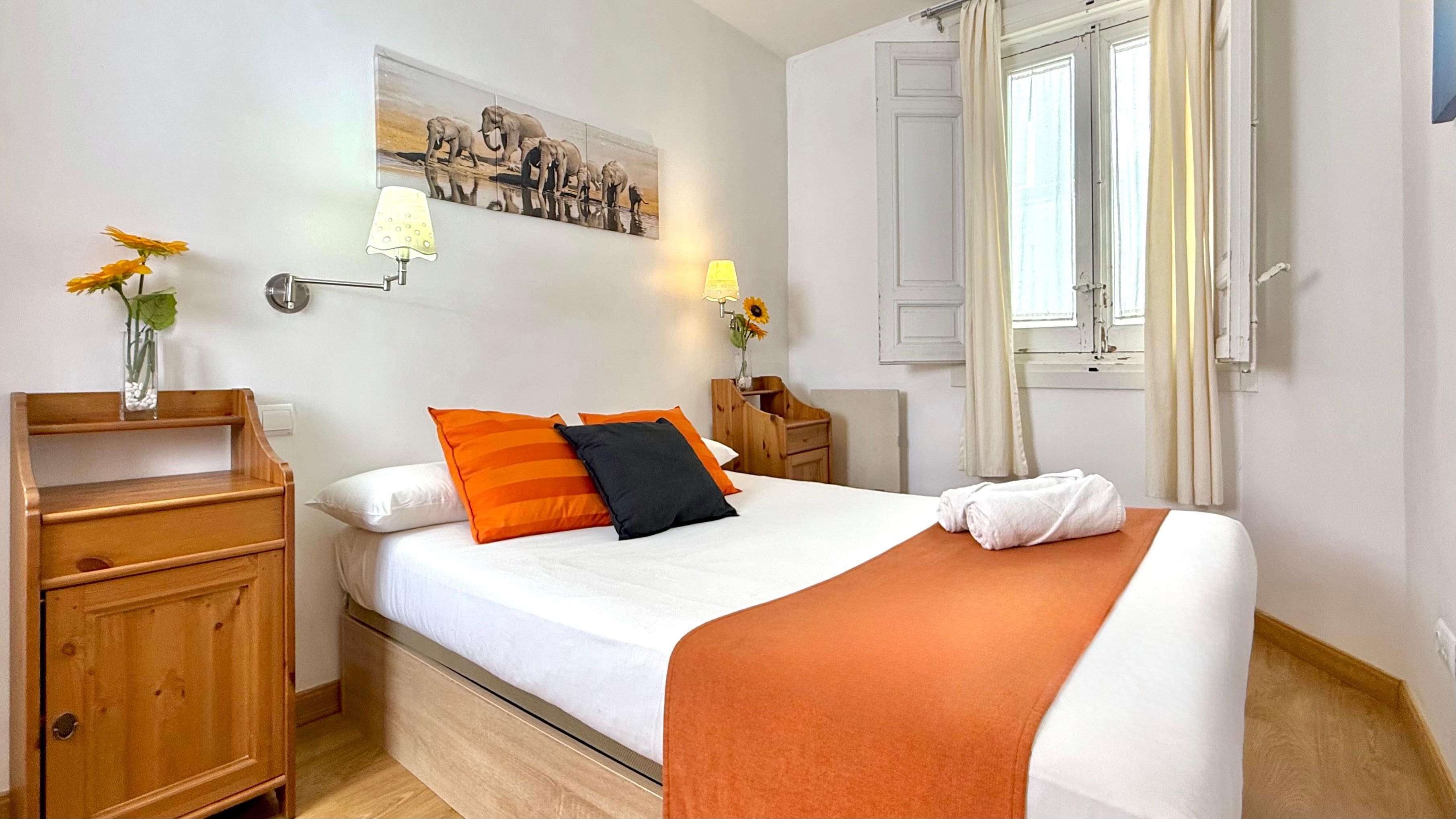 A hotel room with a bed, a nightstand, a lamp, a painting, and a window with curtains.