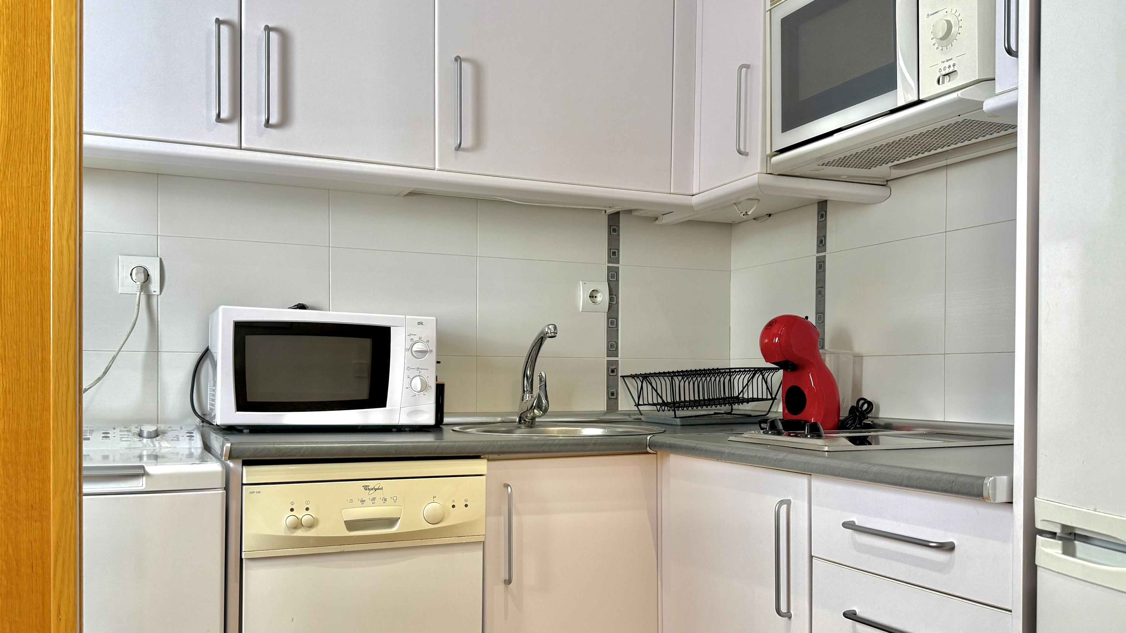 A kitchen with white cabinets, a microwave, a red appliance, and a dishwasher.