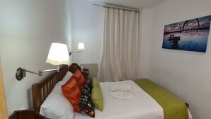 Ett hotellrum med en säng, ett nattduksbord, en lampa, en tavla och ett fönster med gardiner.