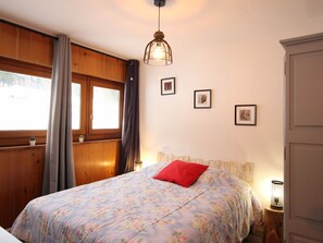A bedroom with a floral bedspread, a red pillow, a wooden headboard, and a hanging light fixture. - Cozy F2 bis 5 pers. in Mont-Dore with parking, near slopes (Mont-Dore)