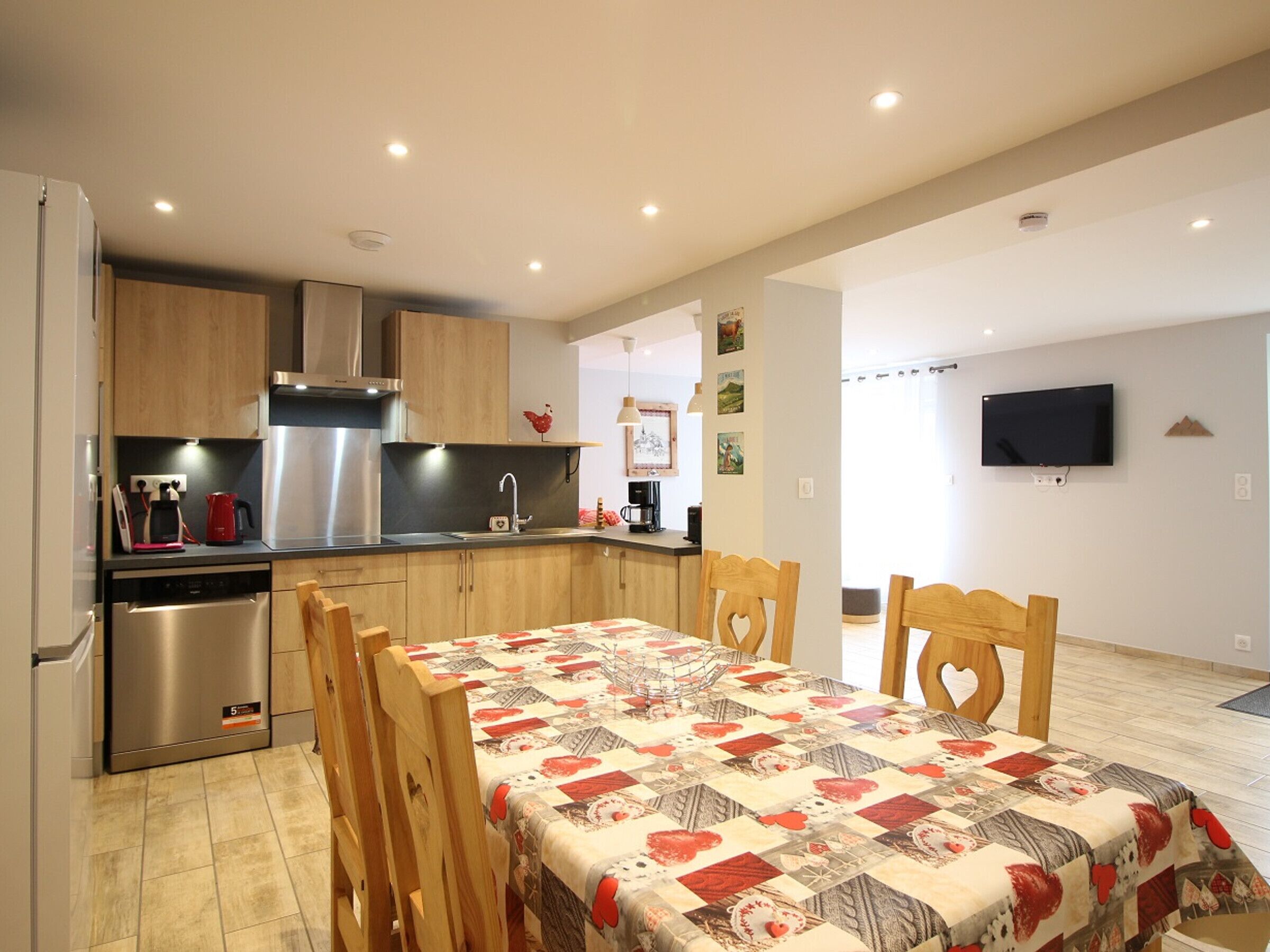 A compact kitchen with modern appliances, a dining area with a quilted tablecloth, and a flat-screen TV mounted on the wall.