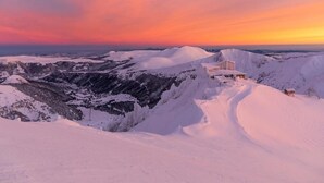 Eine verschneite Berglandschaft bei Sonnenuntergang, bewölkter Himmel.
