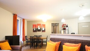 Ein Wohnzimmer mit einer Couch, einem Esstisch mit Stühlen und einer Küchenzeile inklusive Kühlschrank und Mikrowelle.