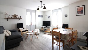 Una sala de estar moderna con un sofá, una mesa de comedor con sillas, un televisor y una araña.