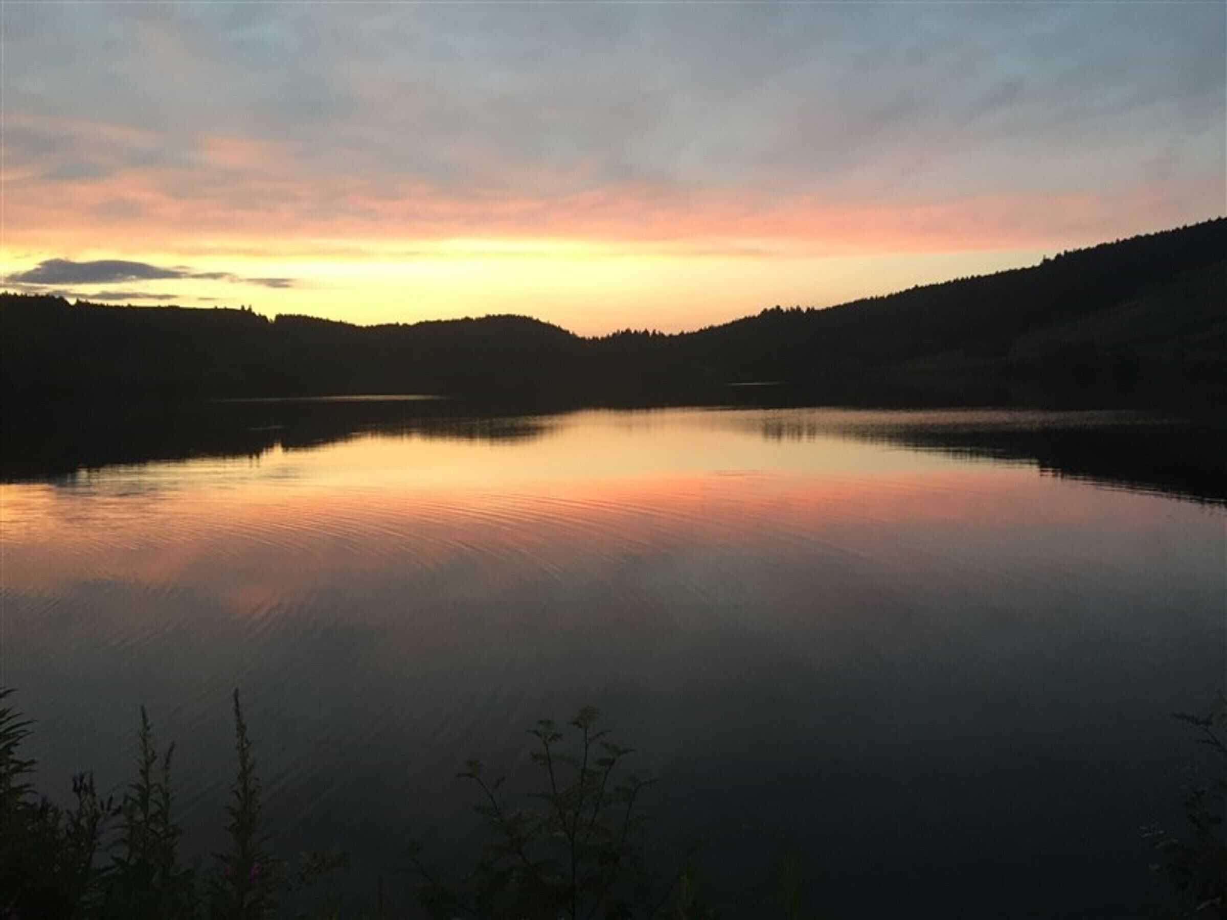 A calm lake at sunset with hills in the background.