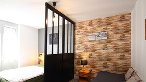 Un dormitorio con cama, mesita de noche con lámpara, pared con diseño de paneles de madera y puerta con listones verticales.
