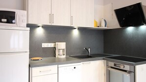 Ett modernt kök med vita skåp, en inbyggd mikrovågsugn, en kaffebryggare, en diskmaskin och en ugn.