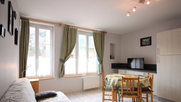 Ett kompakt bostadsutrymme med en soffa, ett matbord med stolar, en tv och ett köksområde.
