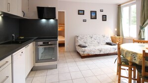 Ett kompakt kök med moderna vitvaror, en soffa med ett mönstrat tyg och en matplats med ett bord och stolar.