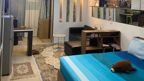 Habitación de hotel compacta con cama, escritorio, silla, sofá, mesita y zona de kitchenette.
