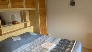 Een slaapkamer met een bed, een houten hoofdbord, een klein nachtkastje en een aan de muur hangend schilderij.