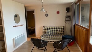 Een knus leefruimte met een bank, twee stoelen, een kleine tafel en een raam met gordijnen.