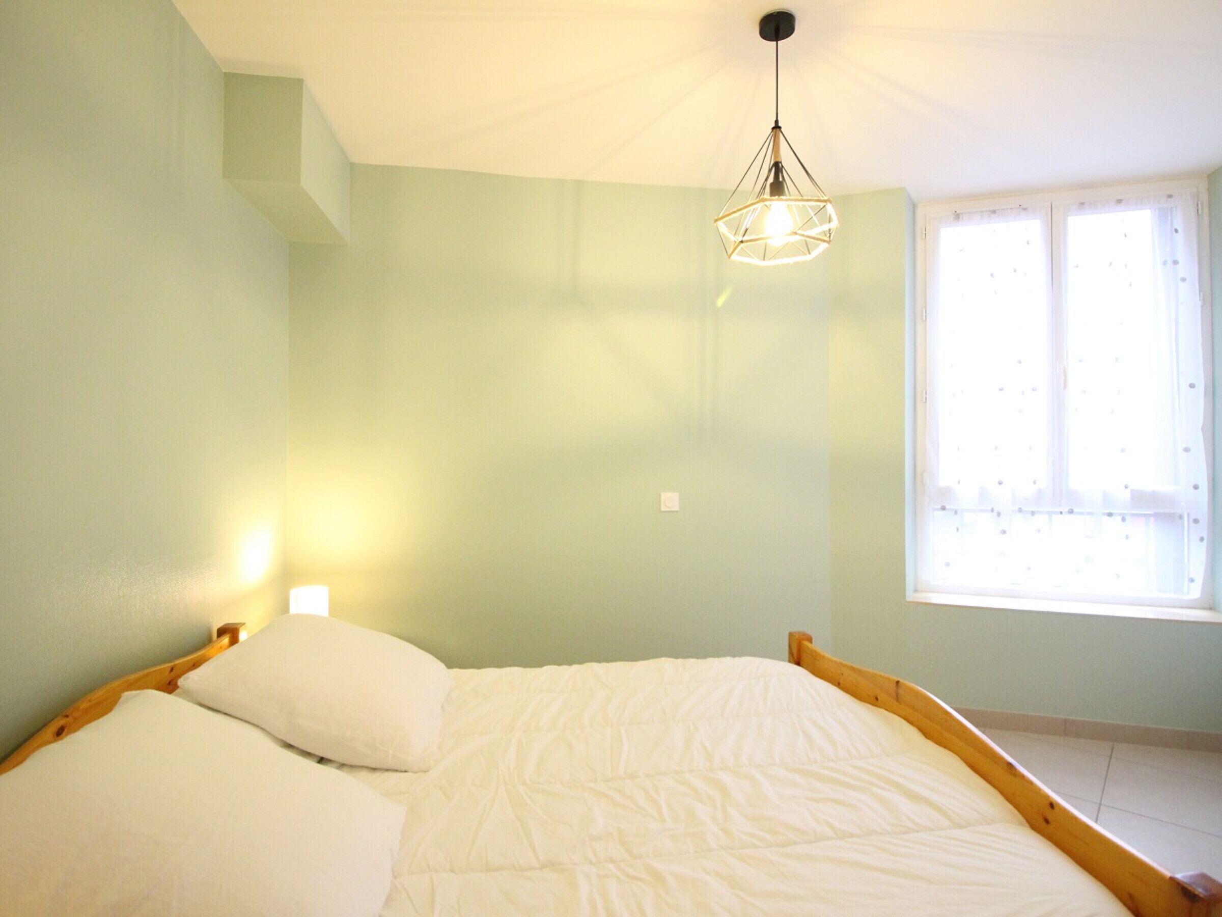 Un dormitorio con cama, lámpara colgante y ventana con cortinas.