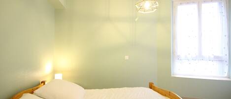 Un dormitorio con cama, lámpara colgante y ventana con cortinas.
