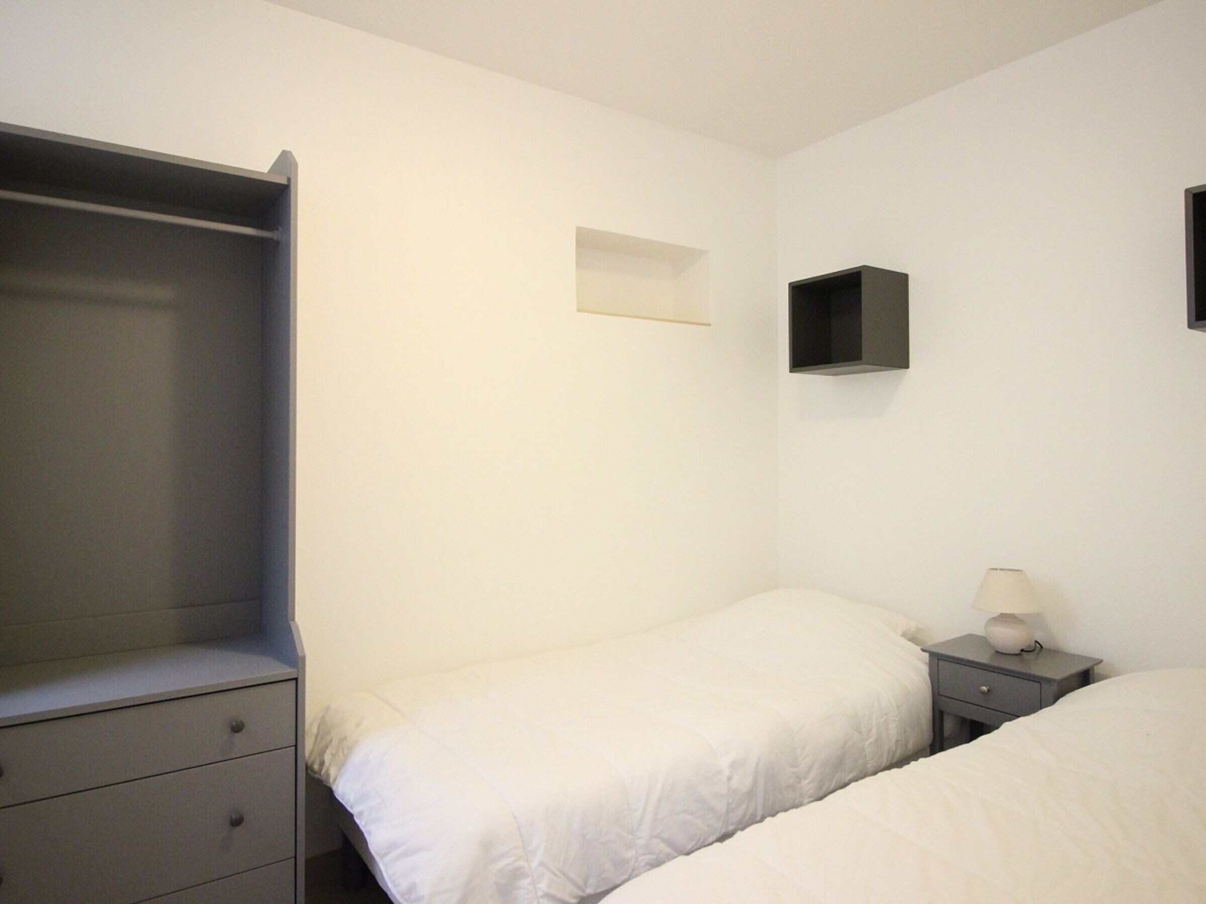 A bedroom with a single bed, a nightstand with a lamp, a dresser, and a wardrobe.