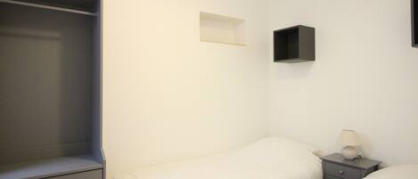 A bedroom with a single bed, a nightstand with a lamp, a dresser, and a wardrobe.