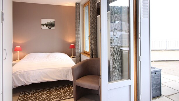 Ett hotellrum med en säng, två sänglampor, en stol, en mönstrad matta och ett fönster med mönstrade gardiner.