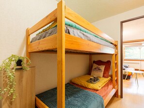 Un llit superposat amb estructura de fusta, un matalàs verd i una almoçada groga. Hi ha una petita planta sobre una prestatgeria de fusta al costat del llit.